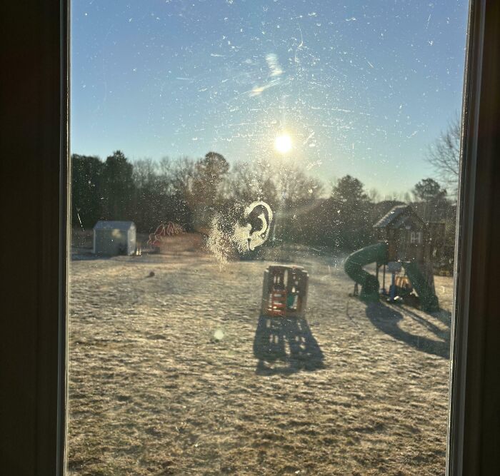 Smudged window with an eerie face-like mark, overlooking a playground at sunrise, creating a creepy and weird atmosphere.