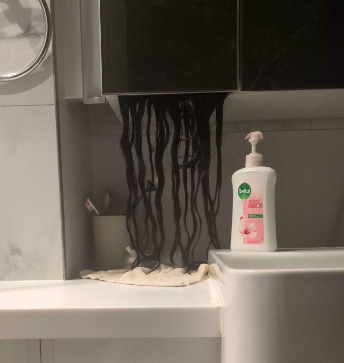 Creepy and weird photo of black hair strands hanging from a bathroom cabinet above a sink with soap dispenser nearby.
