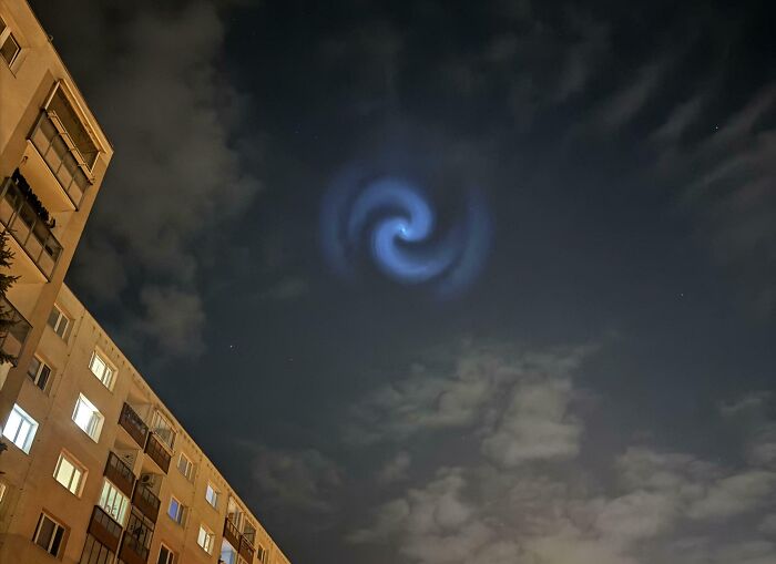 Spiral light in the night sky above apartment buildings creating a creepy and weird photo with eerie atmosphere.