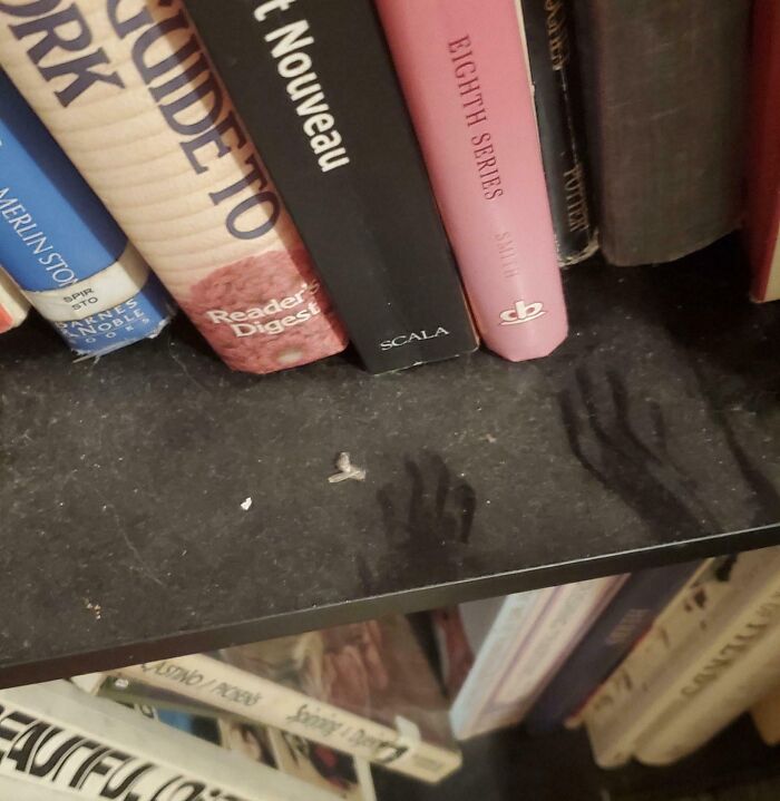 Dusty bookshelf with eerie shadow hand shapes, creating a creepy and weird photo effect to give the heebie-jeebies.