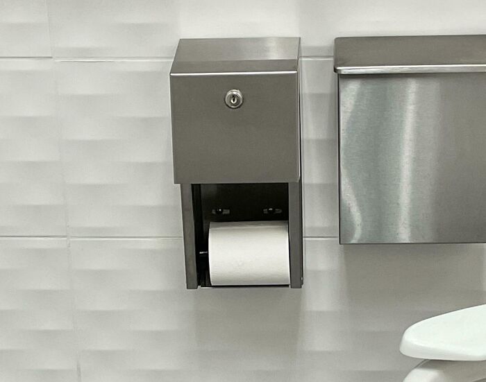 Metal toilet paper dispenser with unusual locking mechanism in a clean bathroom, creepy and weird photo for heebie-jeebies theme.