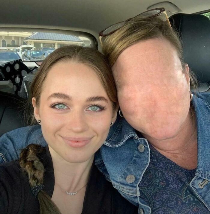 Young woman smiling next to a person with a distorted, creepy faceless appearance in a car selfie, weird photo.