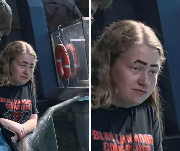 Person with crazy eyebrows drawn thick and angular, seeming to live their own lives on their face, standing by railing.