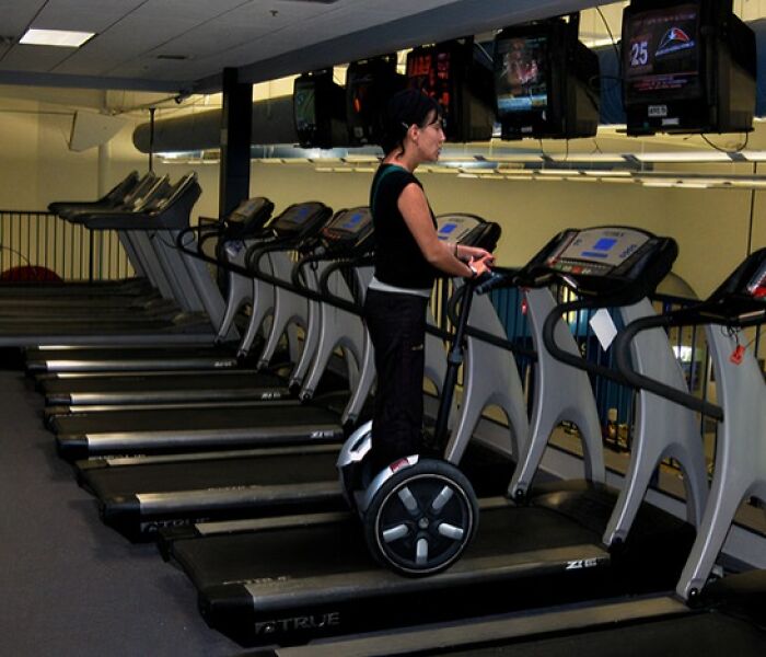 Woman riding a hoverboard on a treadmill at the gym, an unusual and risky gym moment caught on camera.