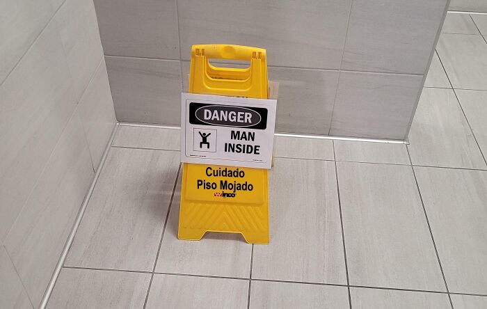 Yellow caution sign with a "Danger Man Inside" warning on tiled gym floor, illustrating gym fails and Darwin Award contenders.