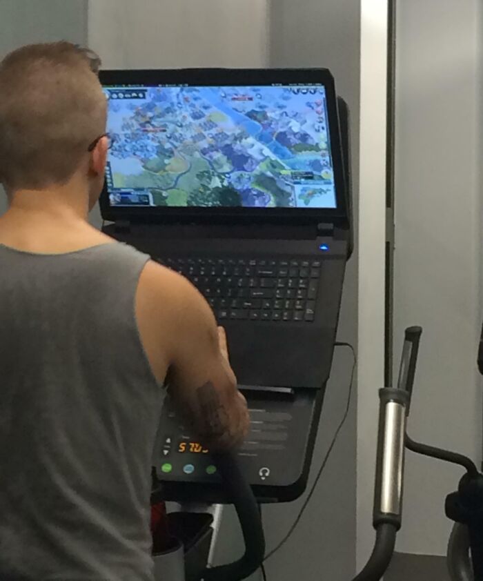 Man using treadmill at gym while playing video game on laptop, an unexpected gym moment caught on camera.