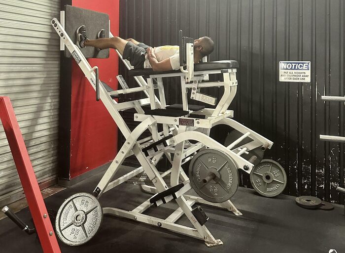 Man lying backwards on gym leg press machine in unusual position, highlighting Darwin award contender gym moments.