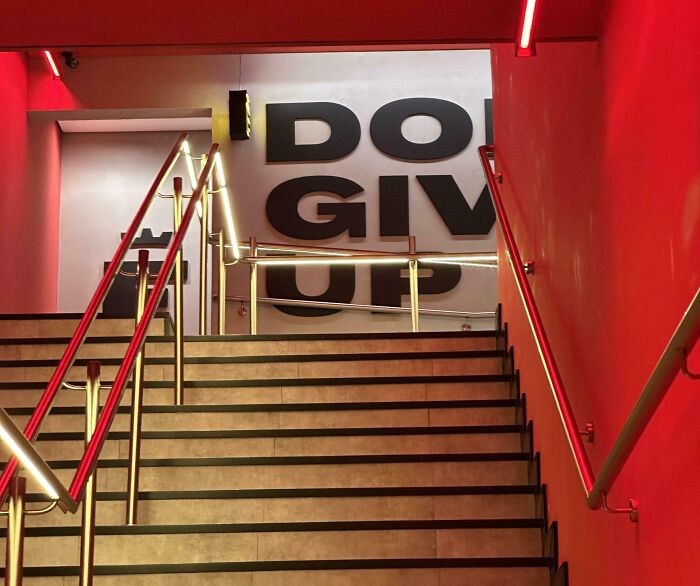 Staircase with red lighting leading to a wall with bold gym motivational text about not giving up.