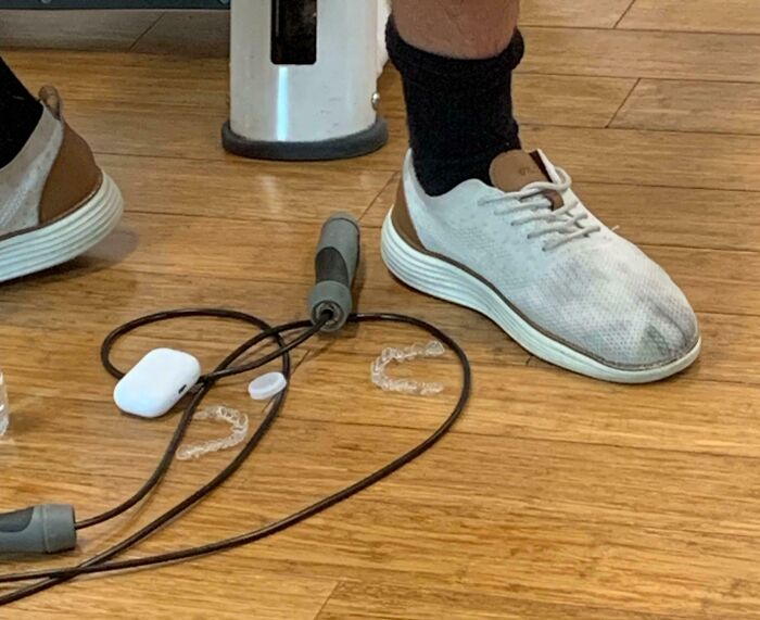 Close-up of dirty gym shoes on wooden floor next to jump rope and clear dental mouthguards, gym fail moments.