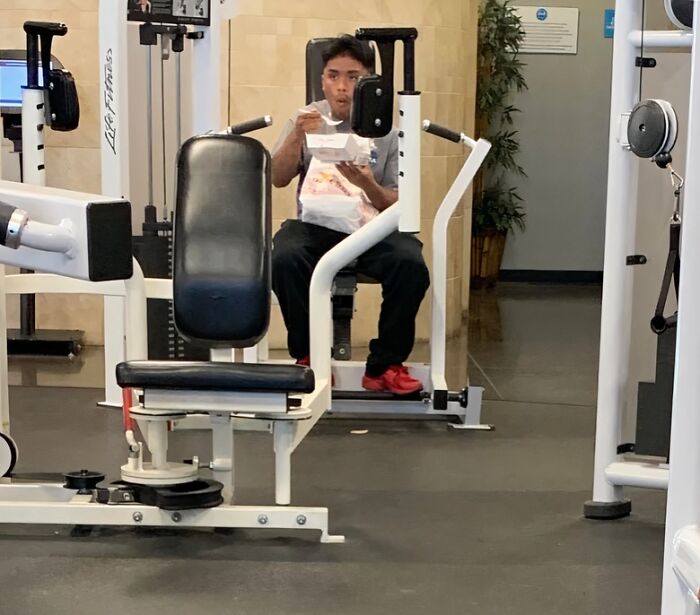 Man eating food while sitting on gym equipment, a surprising moment at the gym, a Darwin Award contender.