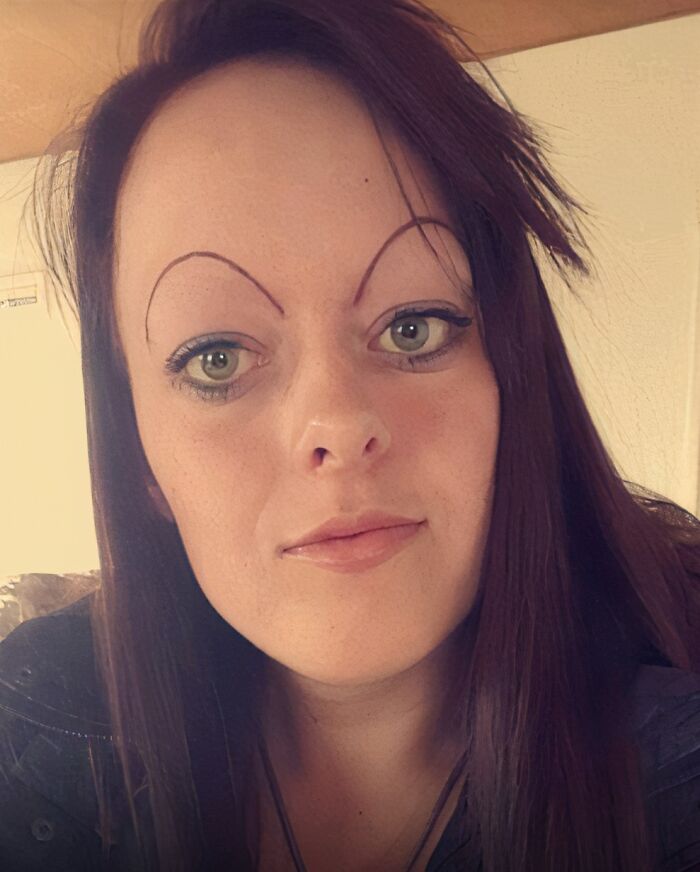 Woman with drawn-on crazy eyebrows that appear to live their own lives on her face in a casual indoor setting.