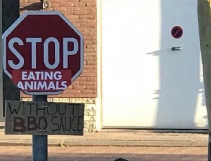 Stop sign altered with funny advice about eating animals without BBQ sauce, creating a humorous and playful street scene.
