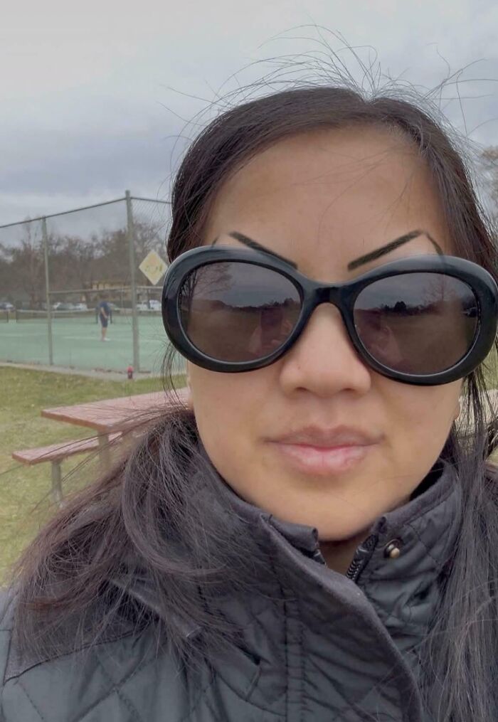 Woman wearing oversized sunglasses with crazy eyebrows seemingly living their own lives on her face outdoors.