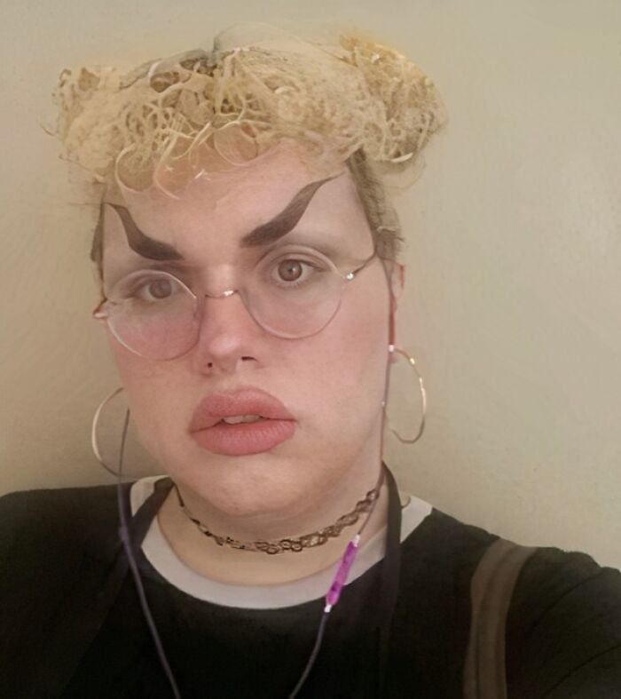Person with crazy eyebrows shaped like thick, upward curves, wearing glasses, hoop earrings, and a lace headpiece.