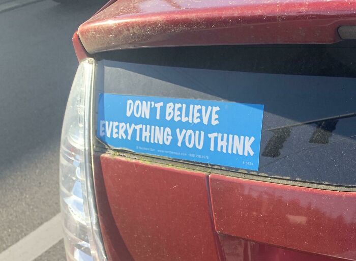 Bumper sticker on red car with funny pieces of advice saying don't believe everything you think in bright daylight.