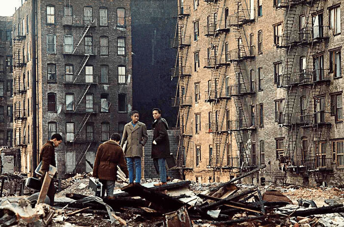 People walking through debris in a worn-down urban housing area