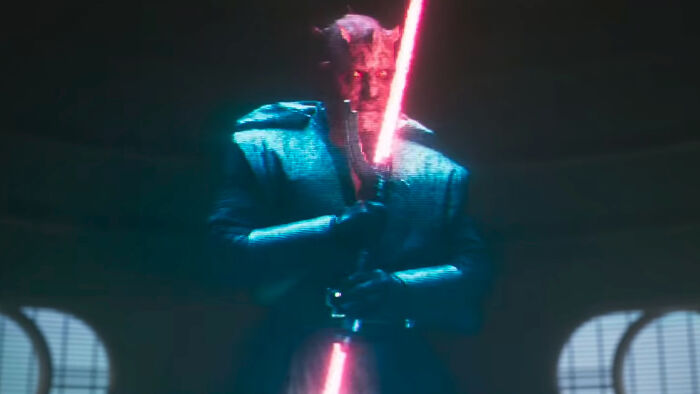 Darth Maul, with red skin and horns, wielding a double-bladed red lightsaber in a dimly lit, futuristic setting. Hilarious movie details.