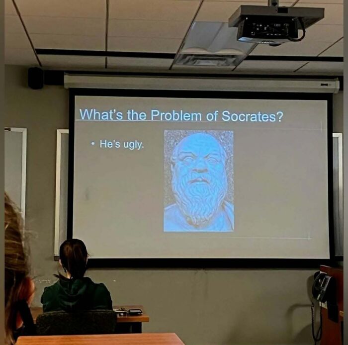 Classroom presentation slide showing a philosophy meme about Socrates with students watching and a projector above.