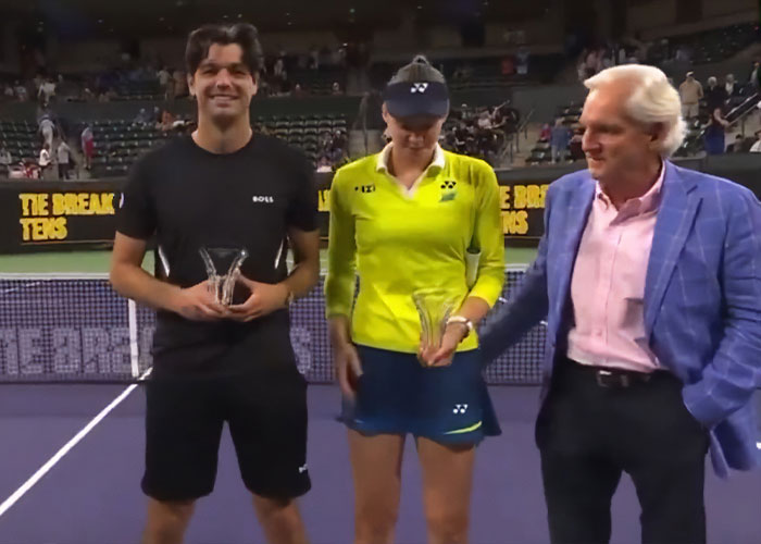 Tennis star Elena Rybakina holding a trophy while awkwardly pushing presenter’s hand away during ceremony.