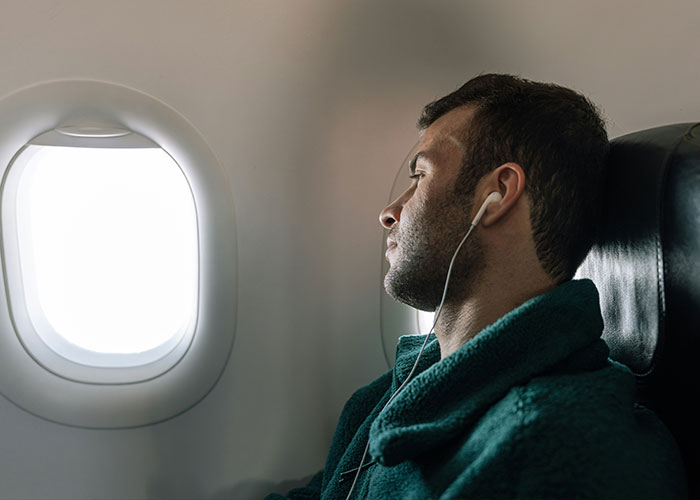 Passenger wearing earphones seated next to airplane window, illustrating major airline's new rule with passenger support.