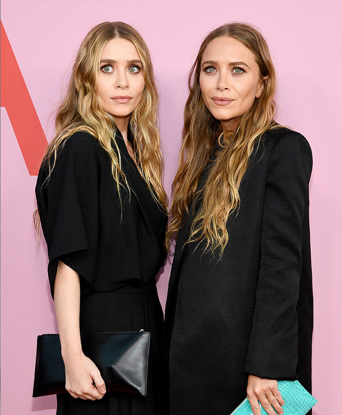 Mary-Kate and Ashley Olsen wearing black outfits holding clutches at an event revealing their disappearance and rift.