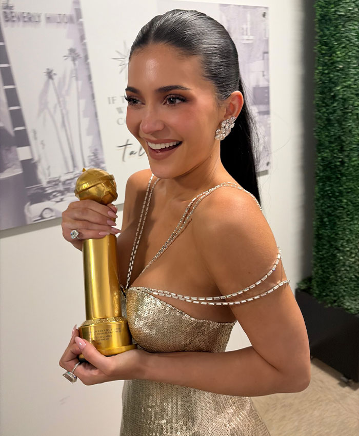 Woman in a gold dress smiling and holding a golden trophy, related to Hollywood rumor about Kylie Jenner and boyfriend’s peers. Woman in a gold dress smiling and holding a golden trophy, related to Hollywood rumor about Kylie Jenner and boyfriend’s peers.