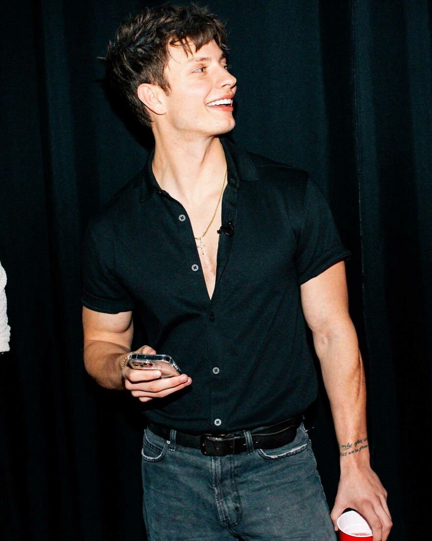 Matt Rife smiling in a black shirt holding a phone and cup, addressing plastic surgery rumors with a casual look. Matt Rife smiling in a black shirt holding a phone and cup, addressing plastic surgery rumors with a casual look.