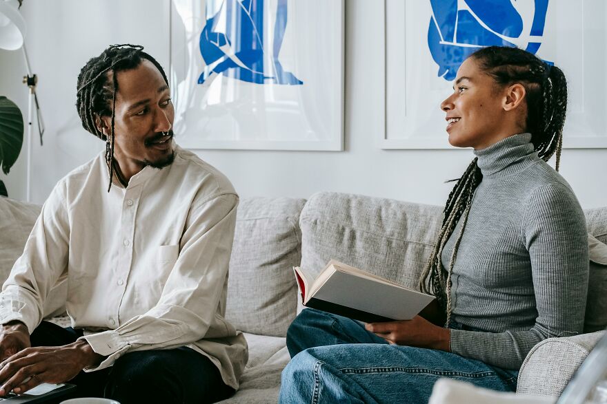 Two people having a friendly conversation on a couch demonstrating small behaviors that make people like you more according to psychologists.