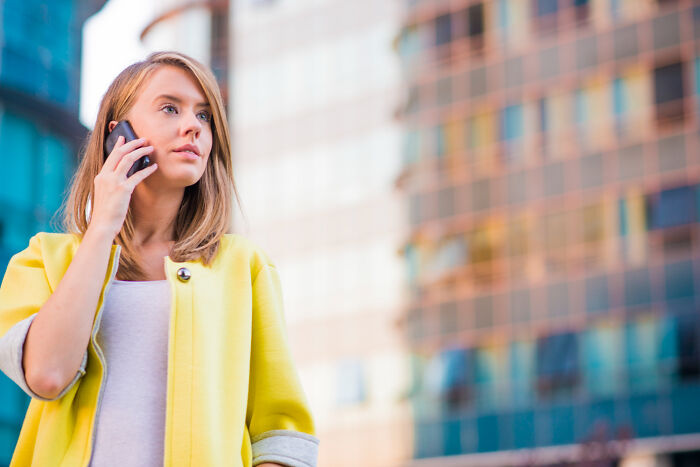 Young woman in yellow coat talking on phone, representing karma striking after people tried to sabotage others.