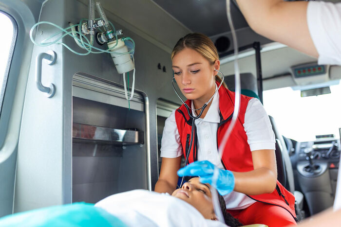 Paramedic wearing a stethoscope and gloves checking patient inside ambulance, illustrating doctors and medical care secrets.