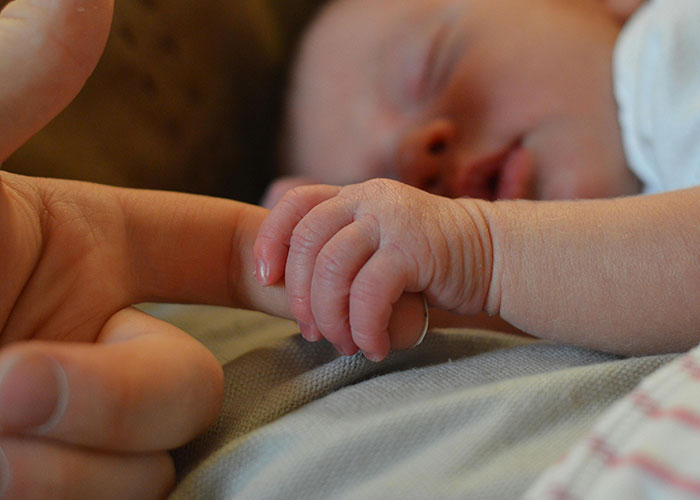 Newborn baby holding man's finger close-up, illustrating caring moments between father and child at home.