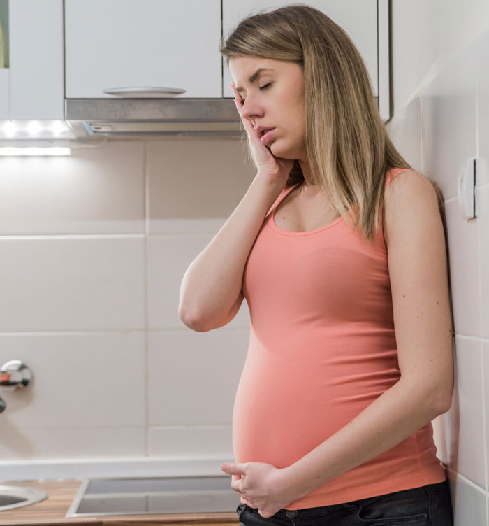 Mulher grávida com uma blusa rosa, segurando a barriga e parecendo angustiada em um ambiente de cozinha moderno. Mulher grávida com uma blusa rosa, segurando a barriga e parecendo angustiada em um ambiente de cozinha moderno.