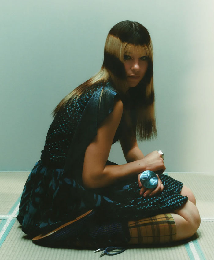 Olympic hero Alysa Liu sitting indoors, wearing a patterned dress and holding a small round object in her hand.