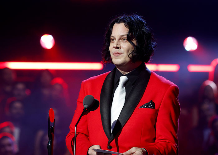 Jack White speaking on stage in a red suit and white tie after Taylor Swift jab sparked major backlash.