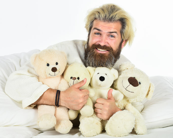 Man with beard holding teddy bears and giving thumbs up, illustrating weird and adorable relationship lessons about men.
