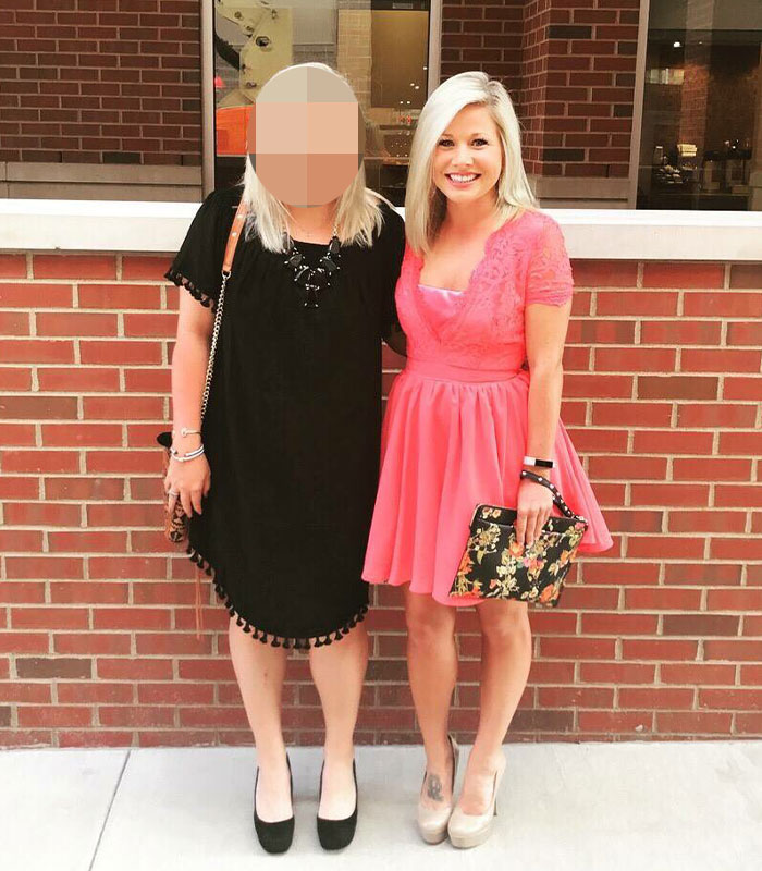 Teacher who went viral for smiling in mugshot poses with friend against a brick wall, wearing a pink dress and holding a purse.