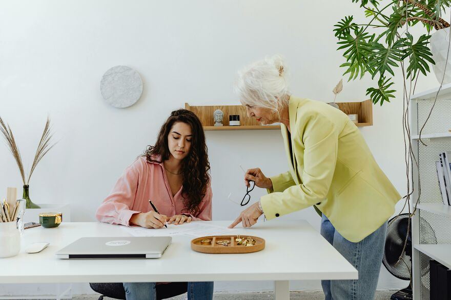 Young woman writing notes while an older woman shares practical psychology tricks in a modern office setting.