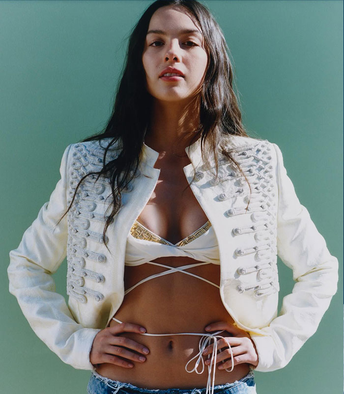 Olivia Rodrigo posing in a white jacket and strappy top, with fans noticing bizarre details on Vogue cover. Olivia Rodrigo posing in a white jacket and strappy top, with fans noticing bizarre details on Vogue cover.
