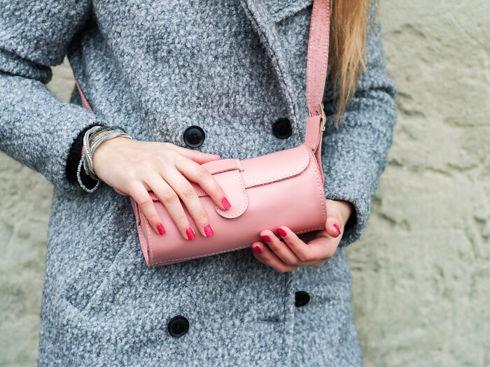 Woman in a gray coat holding a pink handbag, highlighting secrets women don't tell men in everyday life.