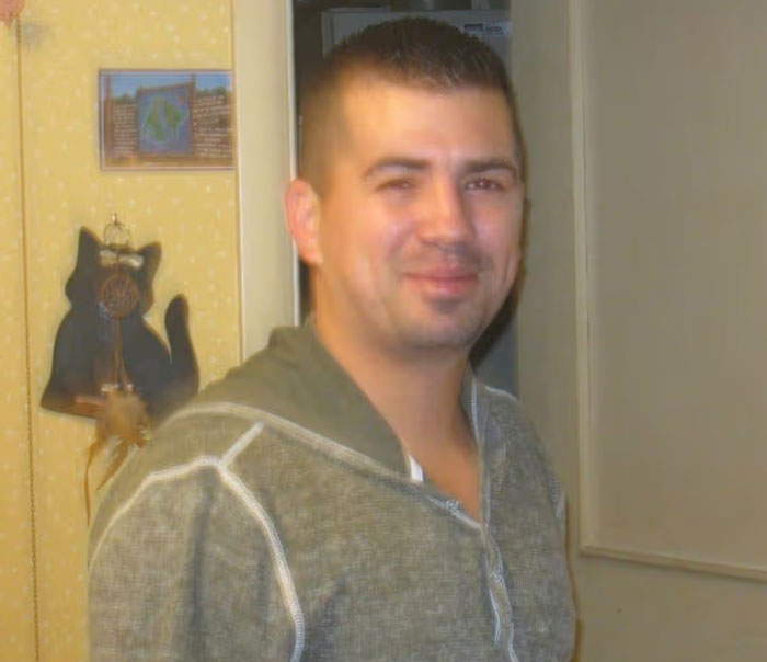 Man in casual green sweater smiling indoors, related to unsettling mysteries that continue to fascinate and disturb.