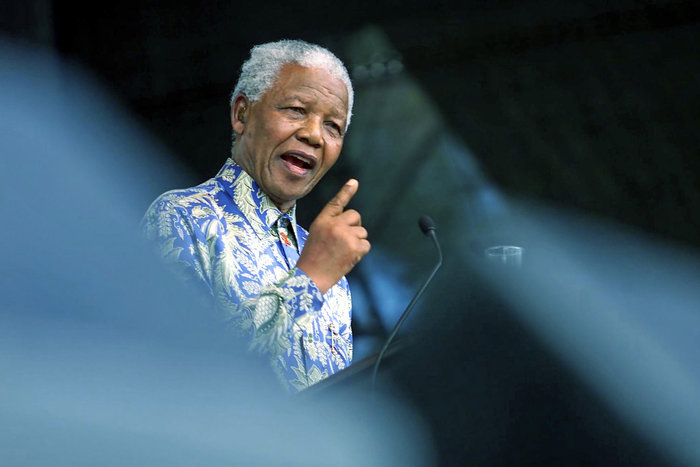 Nelson Mandela speaking at a podium, wearing a patterned shirt, representing famous leaders who changed history.