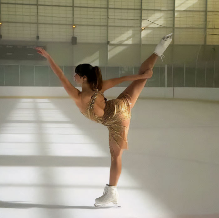 Alysa Liu performing a figure skating move on ice wearing a sparkling gold dress in an indoor rink.