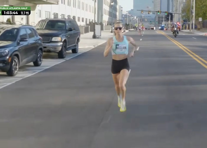 US track star running in city marathon wearing sunglasses and athletic gear amid official race timing and vehicles nearby