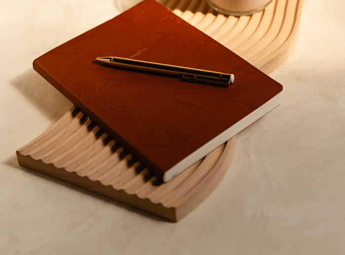 Brown notebook and black pen resting on a textured wooden tray, capturing a calm moment for relationship reflections.