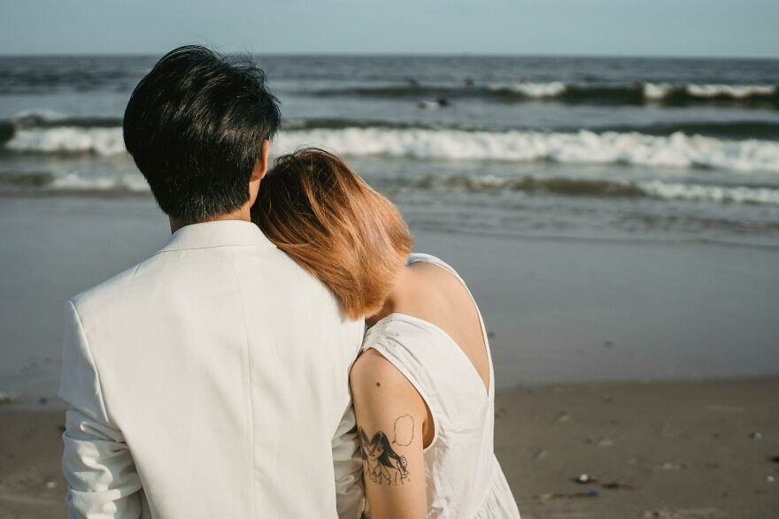 Couple showing small behaviors that make people like you more, sitting closely together by the ocean shore.