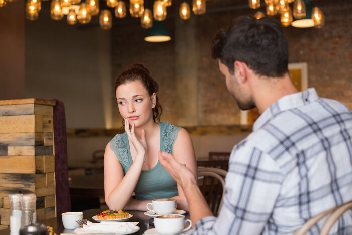 Woman showing discomfort while talking to man in cafe, revealing secrets women don’t tell men in relationships.