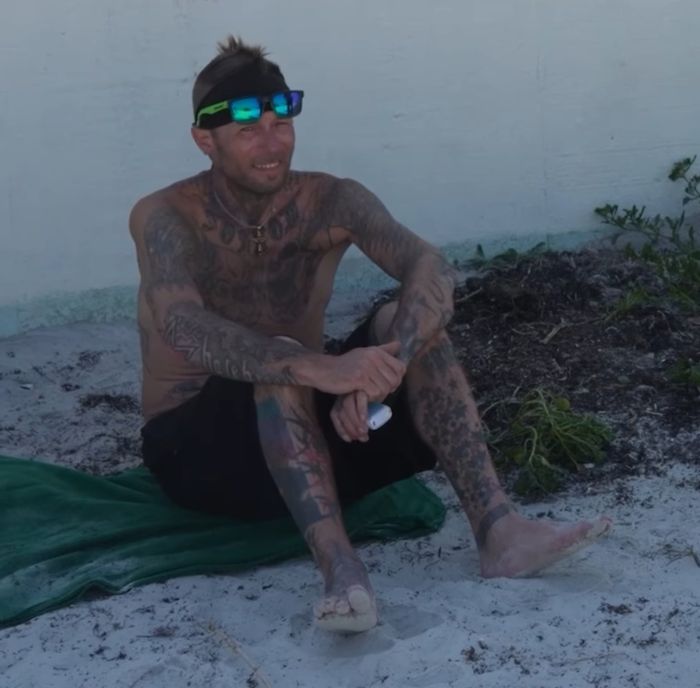 Tattooed man sitting on a towel at Daytona Beach, reportedly found partying with spring breakers during spring break.