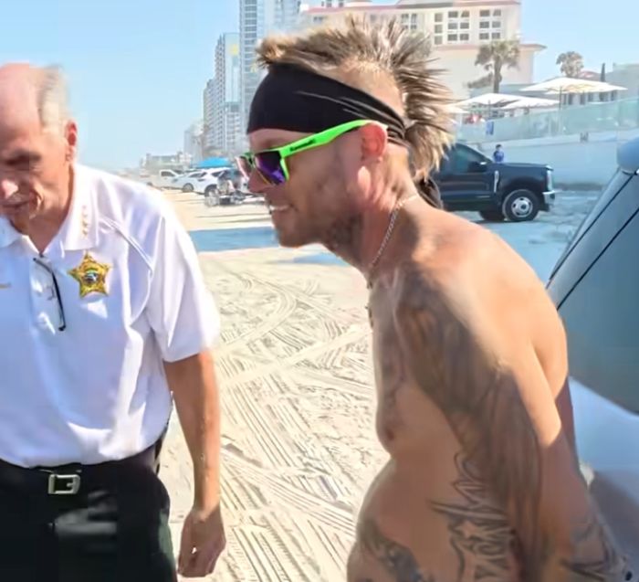 Man with mohawk and tattoos confronted by law enforcement at Daytona Beach during spring break party.
