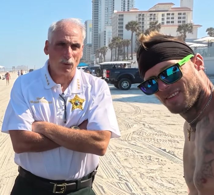 Sheriff talking on Daytona Beach with a young man during spring breakers party amid crime investigation.