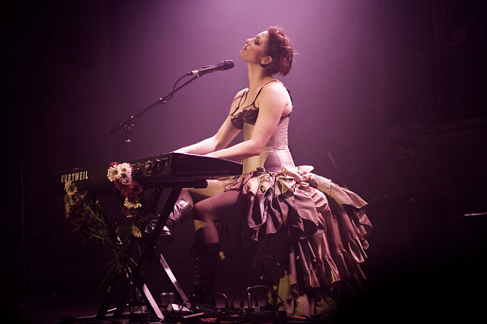 Performer in a dramatic outfit playing keyboard on stage with moody lighting, reflecting on celebrity opinions and changes.